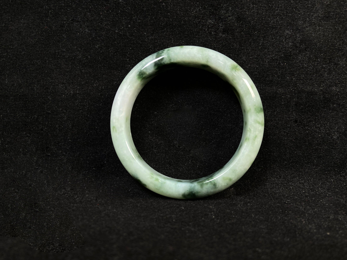 A milky white jade bangle with floating deep and light green patterns.