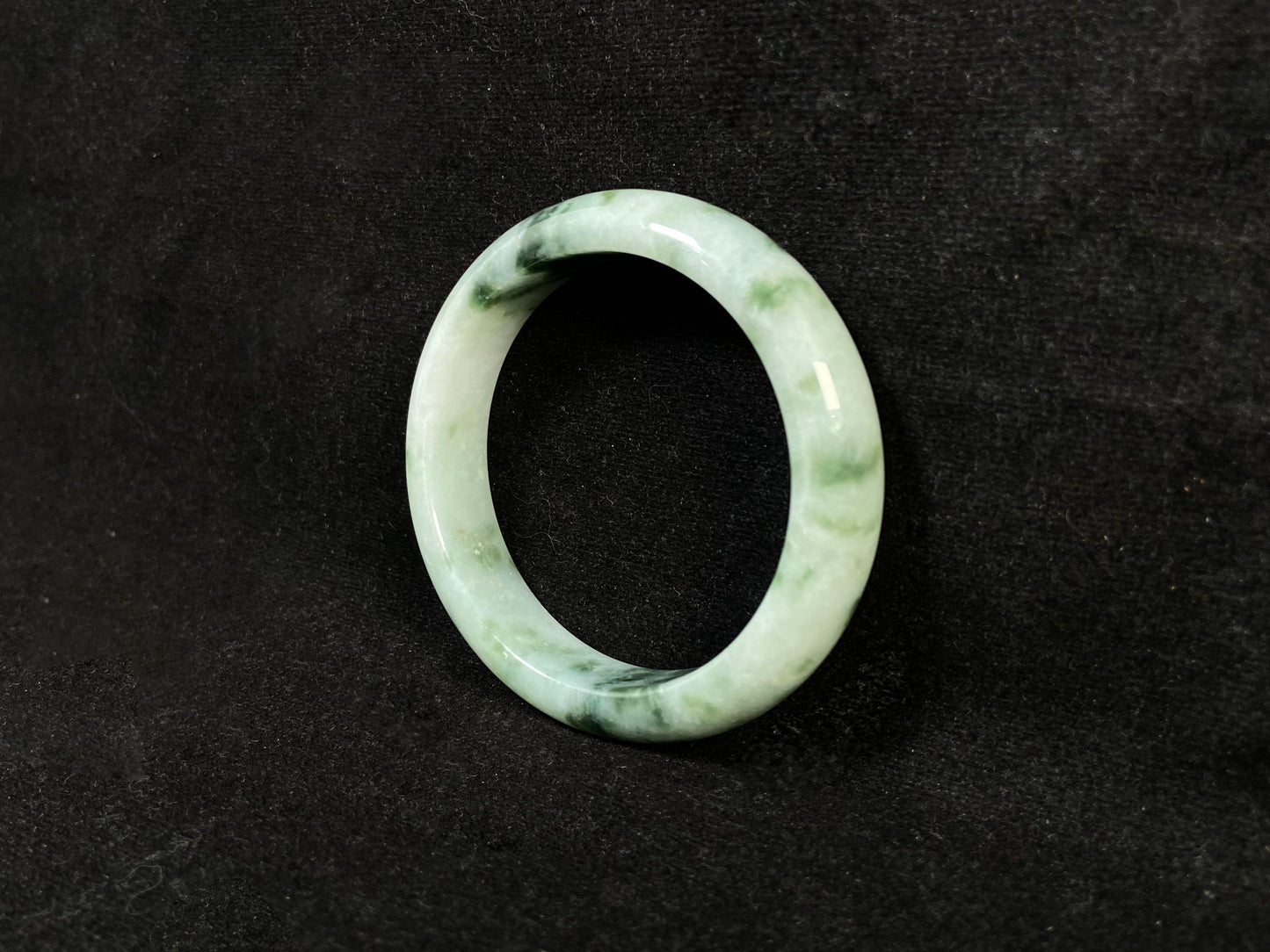 A milky white jade bangle with floating deep and light green patterns.
