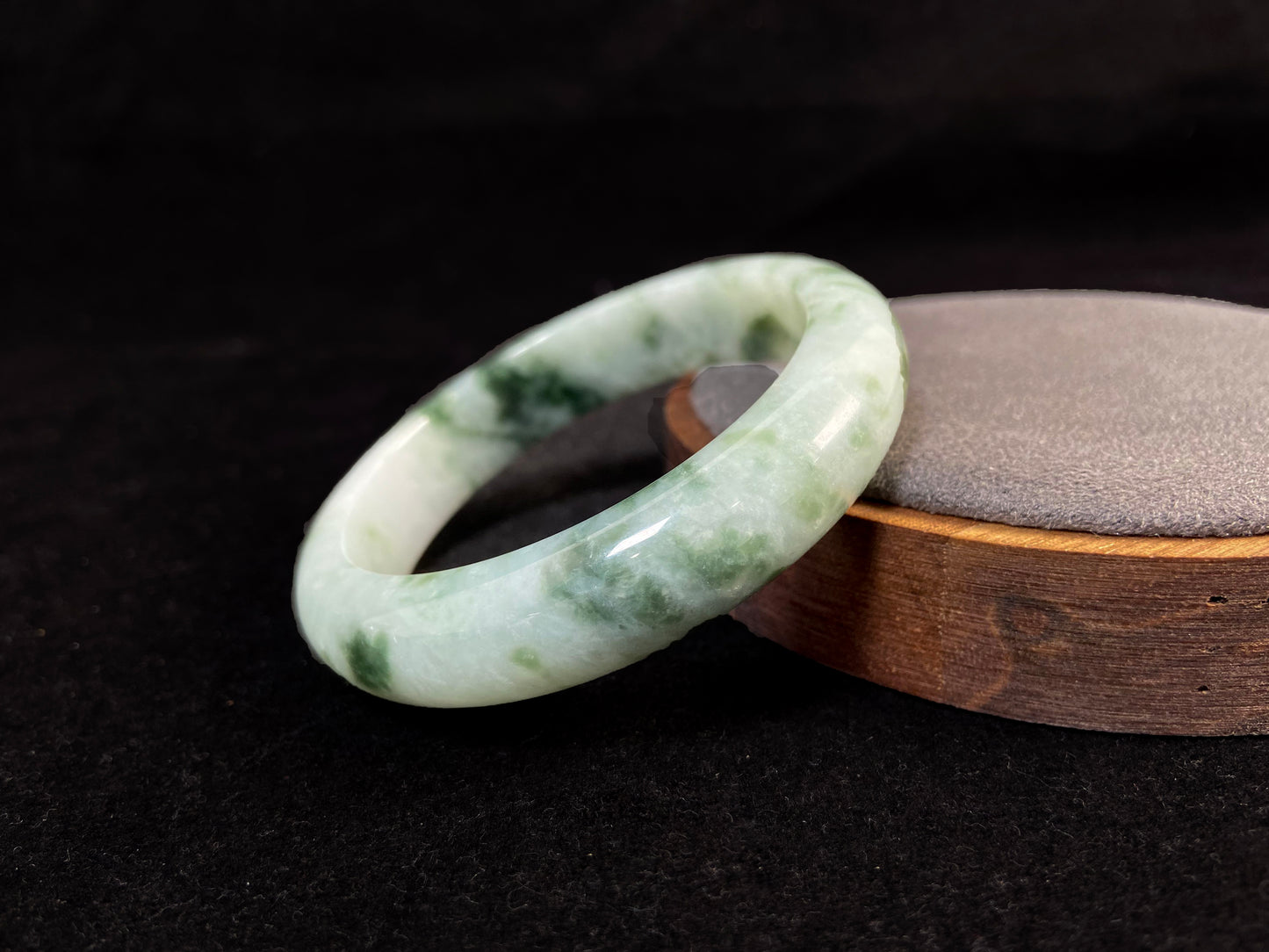 A milky white jade bangle with floating deep and light green patterns.