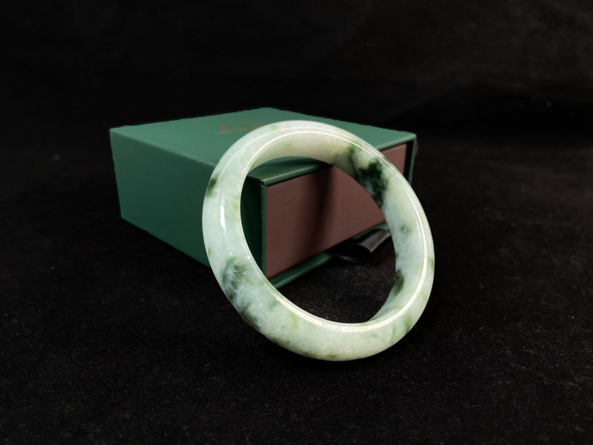 A milky white jade bangle with floating deep and light green patterns.