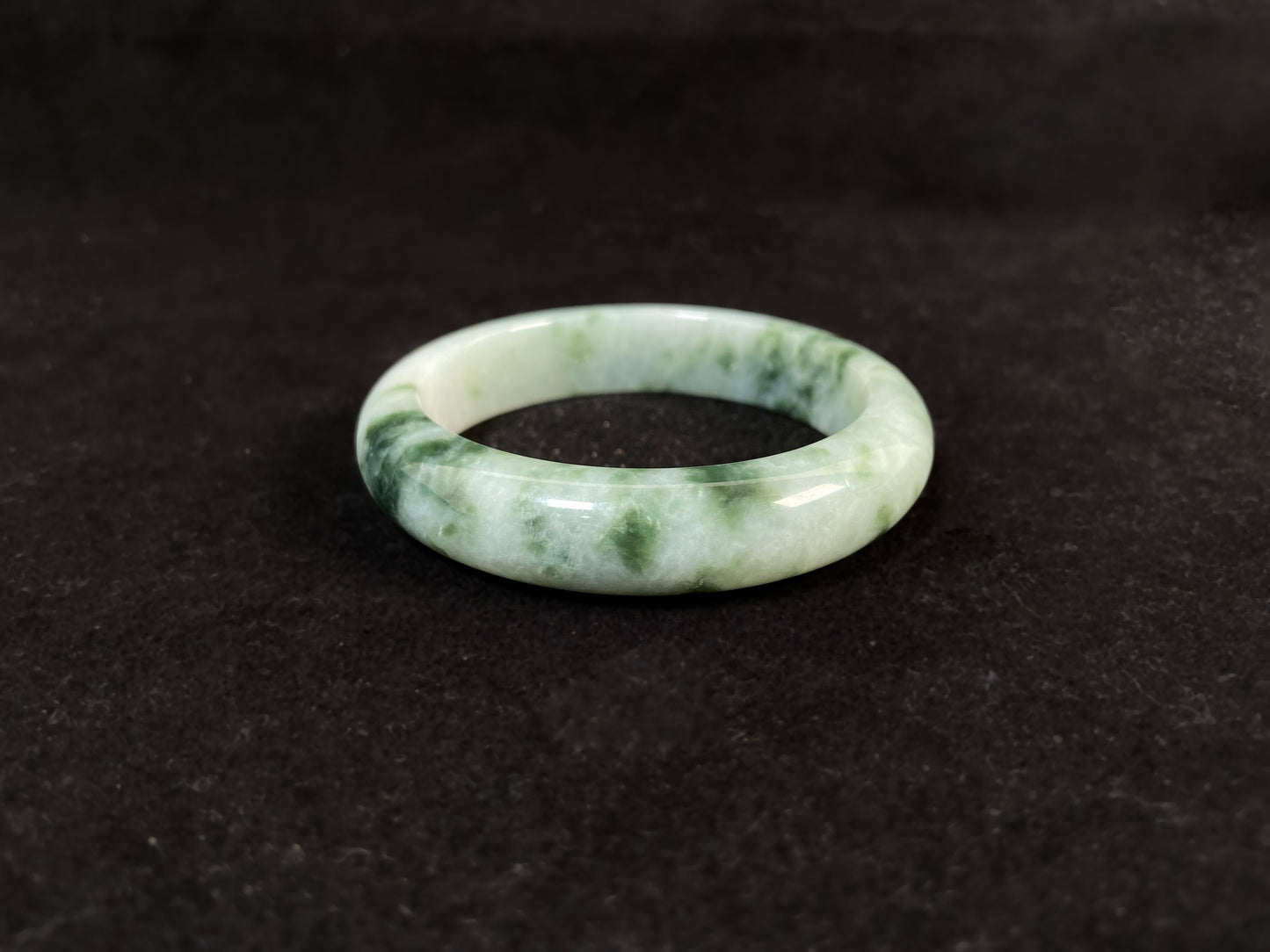A milky white jade bangle with floating deep and light green patterns.