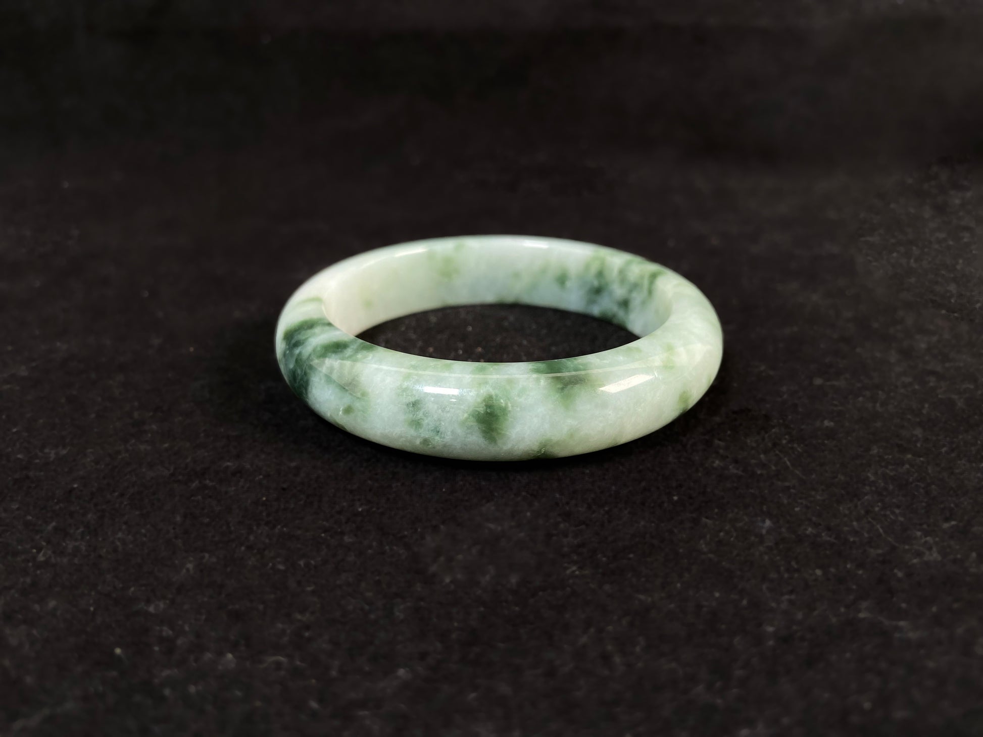 A milky white jade bangle with floating deep and light green patterns.