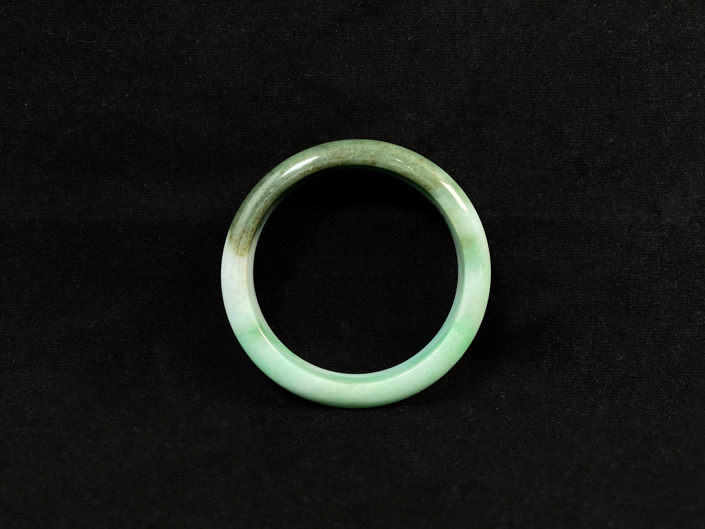 A jade bangle with a milky white base, featuring a large apple green section and a smaller olive green portion.