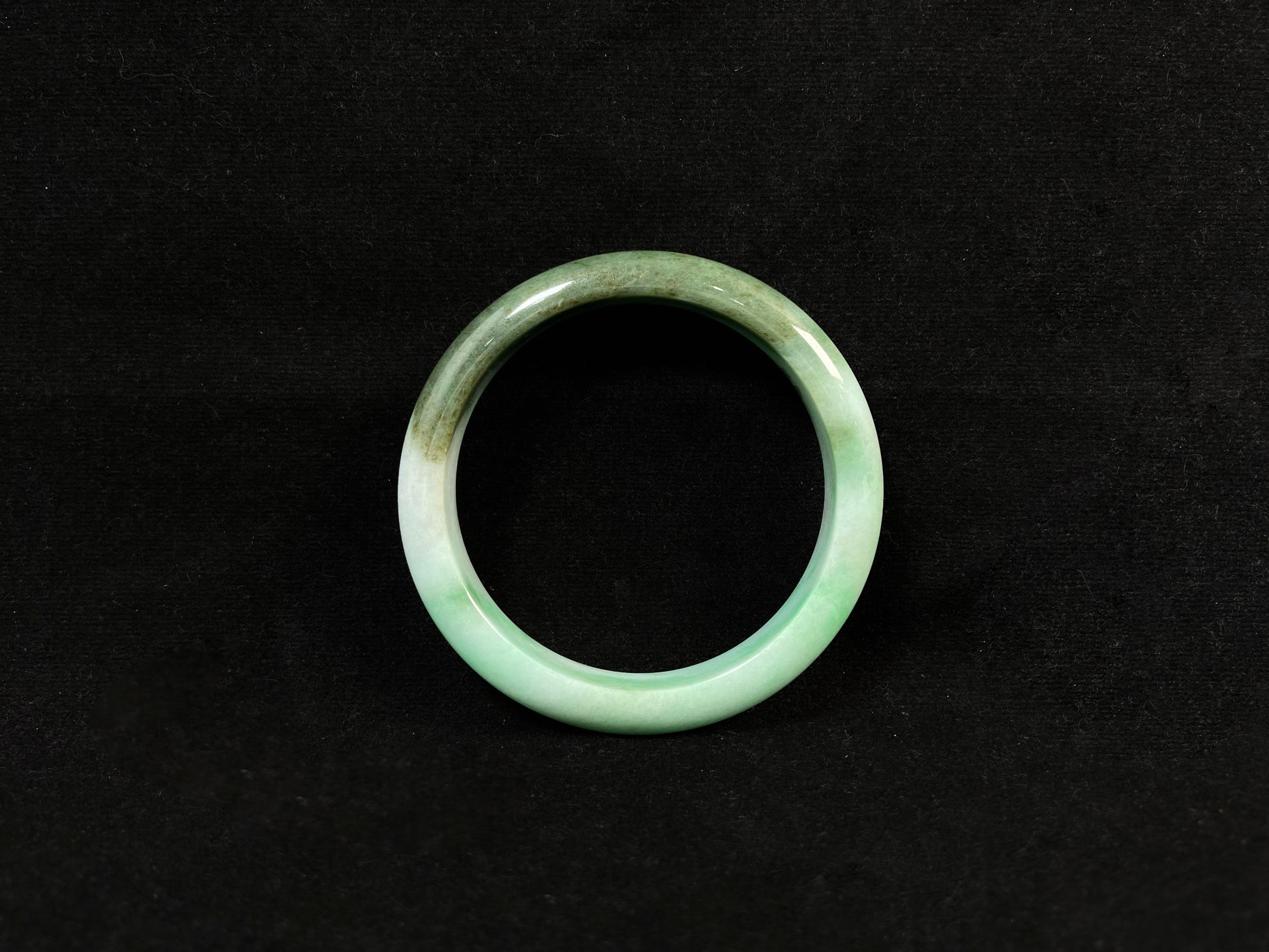A jade bangle with a milky white base, featuring a large apple green section and a smaller olive green portion.