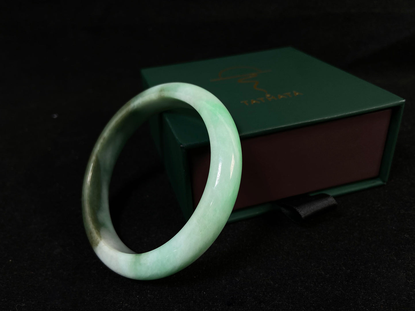 A jade bangle with a milky white base, featuring a large apple green section and a smaller olive green portion.