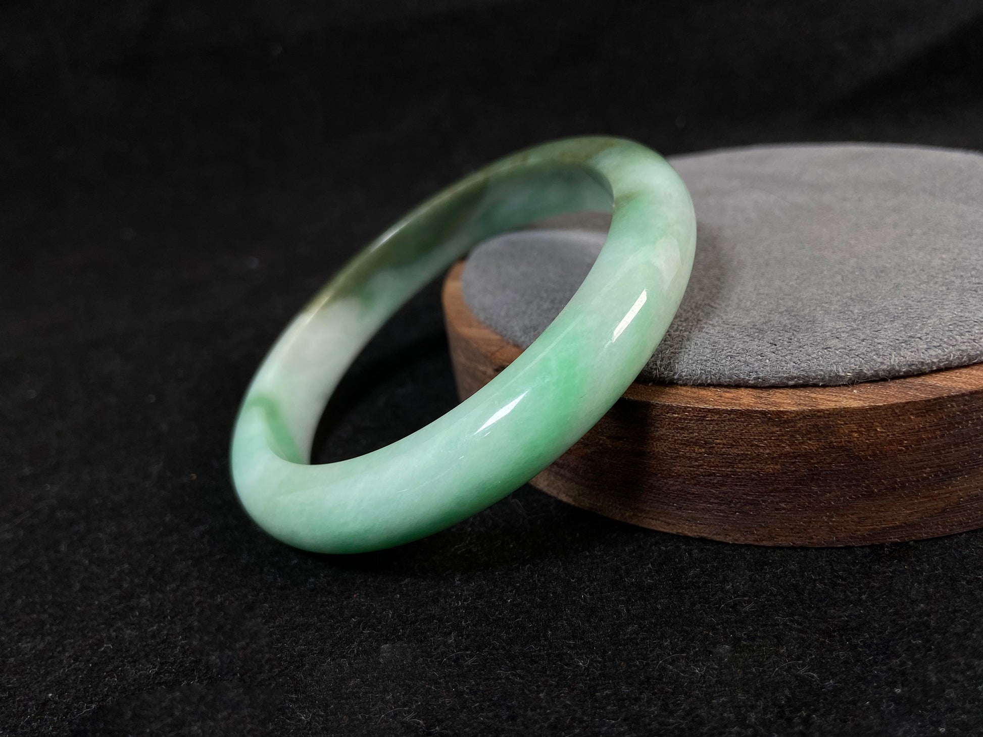 A jade bangle with a milky white base, featuring a large apple green section and a smaller olive green portion.