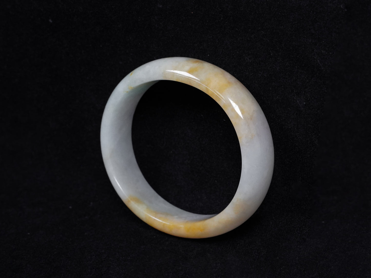 This jadeite bangle features a pale white base with soft green and warm yellow hues blending gently.