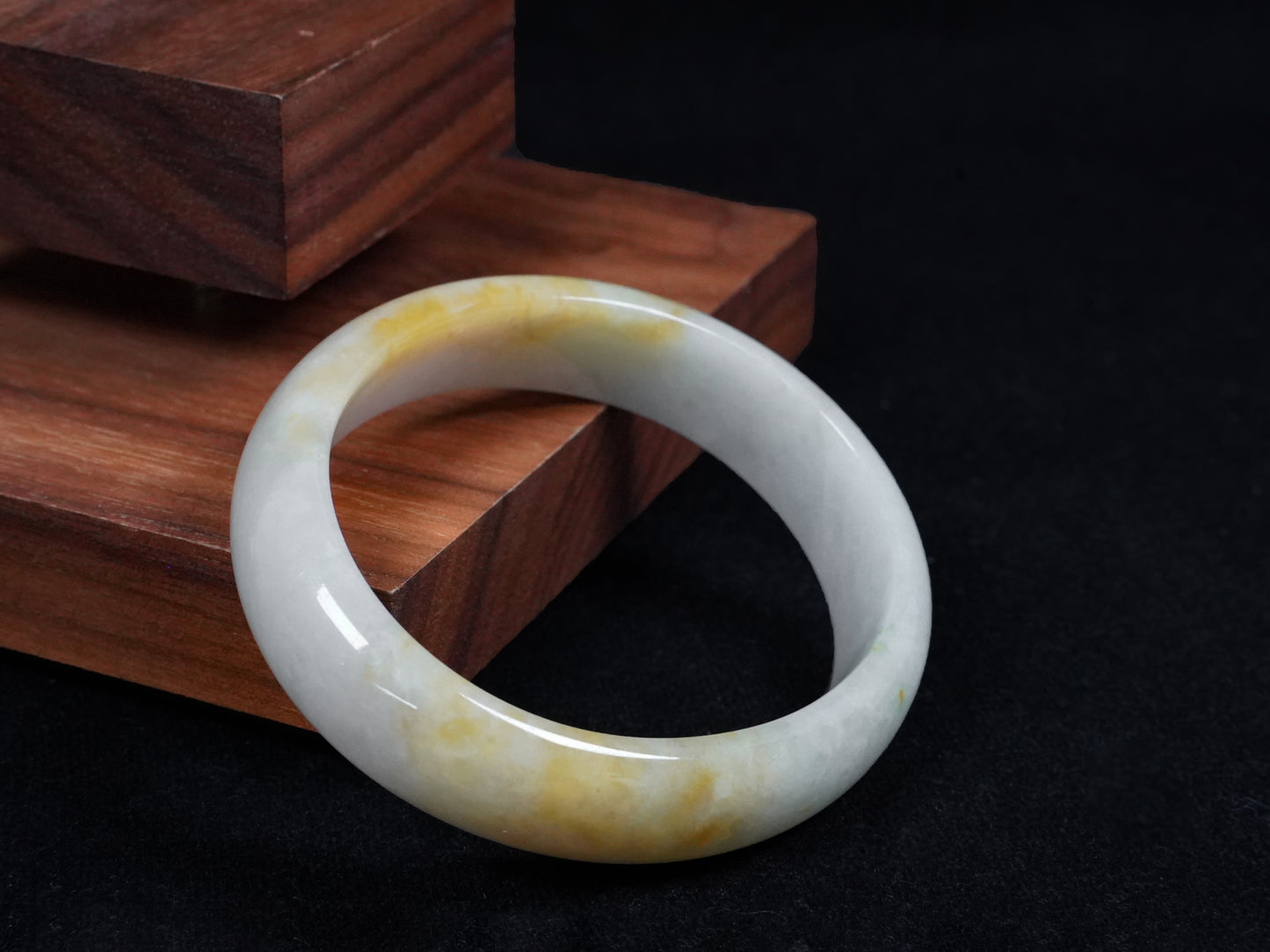 This jadeite bangle features a pale white base with soft green and warm yellow hues blending gently.