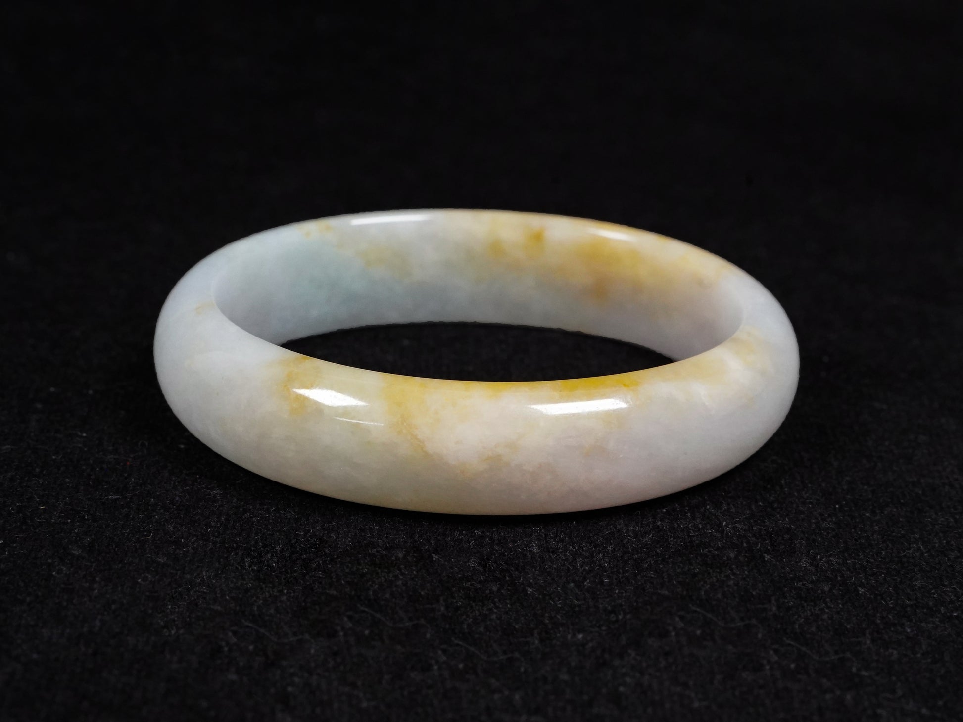 This jadeite bangle features a pale white base with soft green and warm yellow hues blending gently.