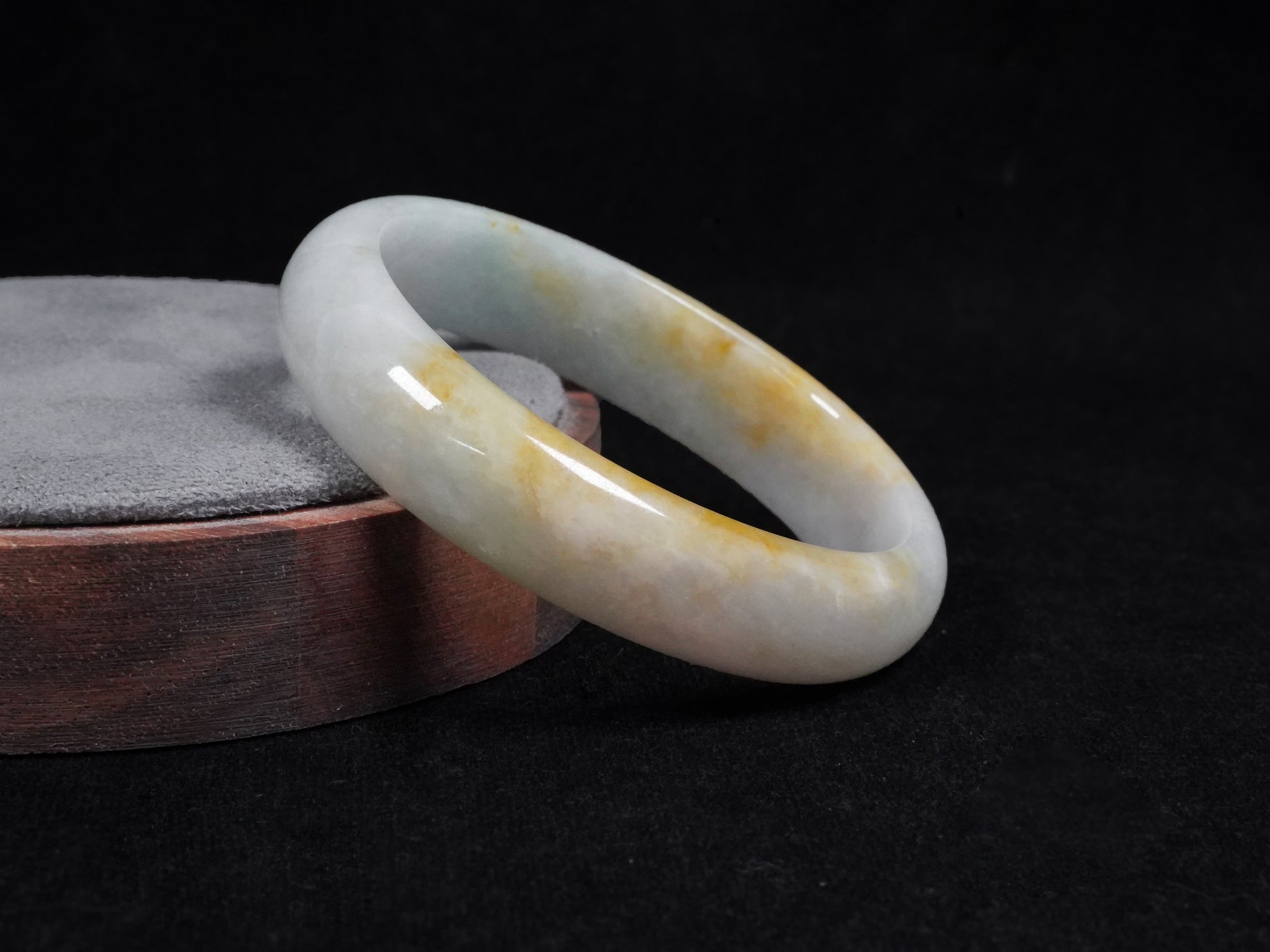This jadeite bangle features a pale white base with soft green and warm yellow hues blending gently.