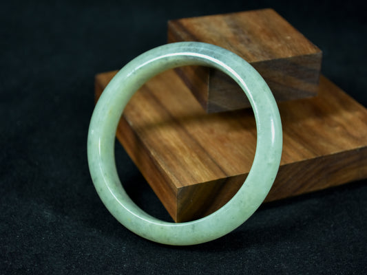 Green jade bracelet on a wooden block against a dark background
