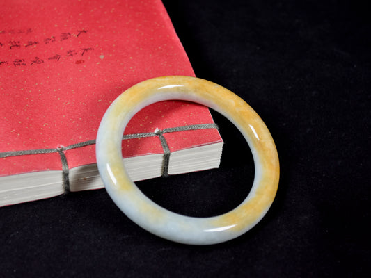 Round jade bracelet on a black background with a red book.