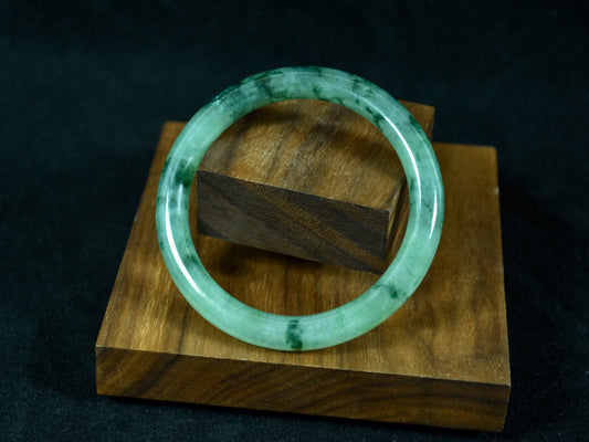 Green jade bracelet on a wooden stand against a dark background