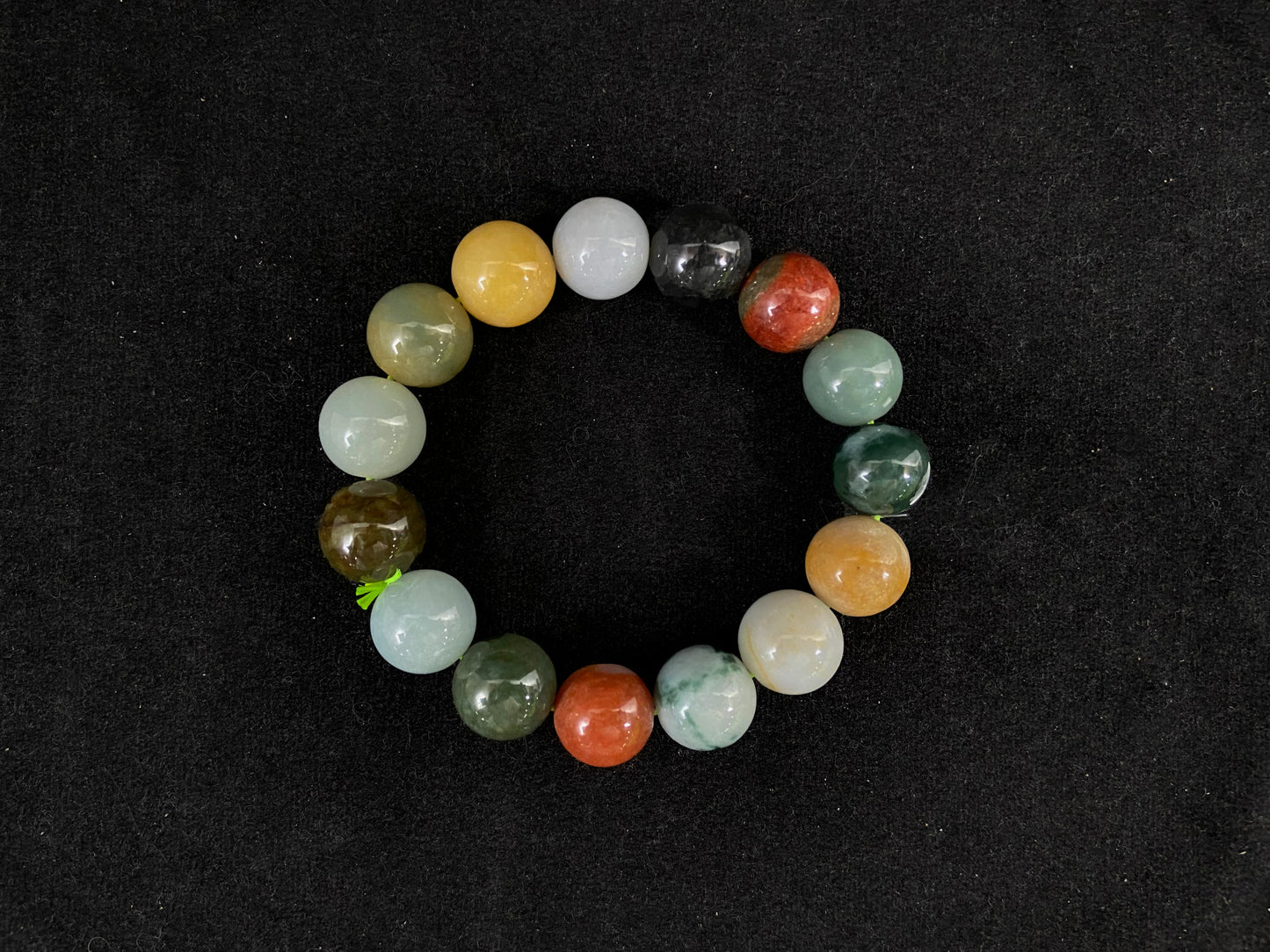 A strand of uniformly sized jade beads in a varied color palette including yellow, reddish brown, and grayish greenish black.