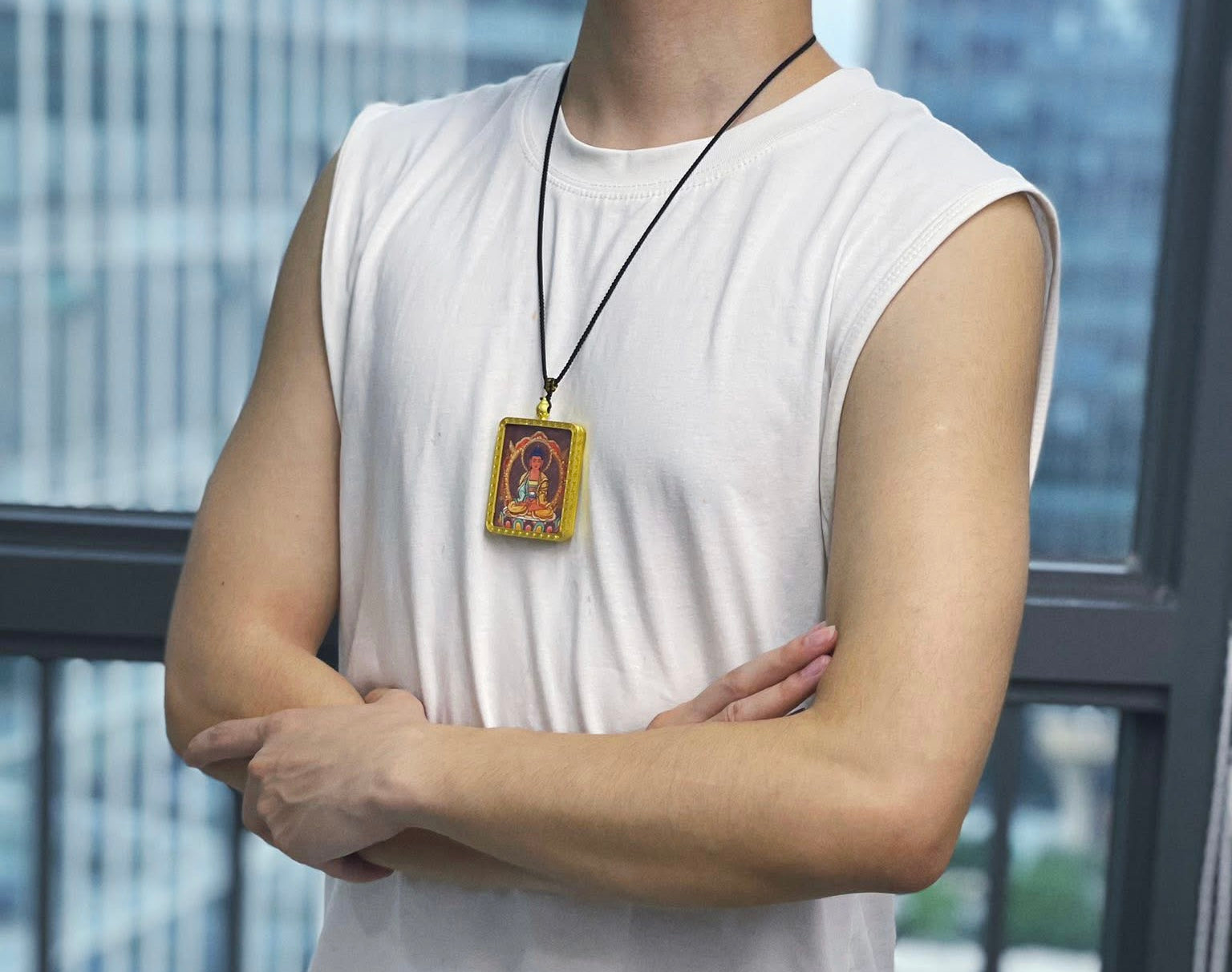 Person wearing a white sleeveless shirt with a necklace featuring a pendant, standing against a blurred cityscape background.