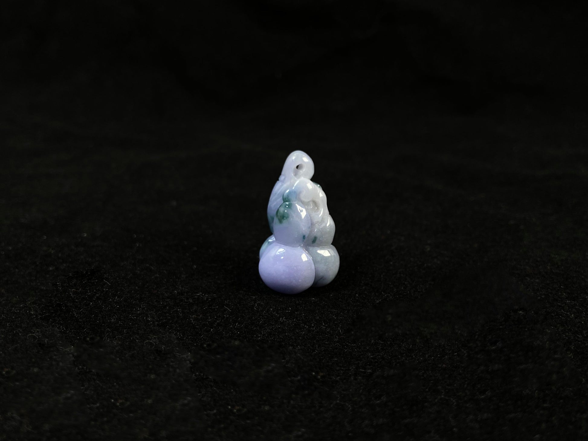 A violet jade carving of three entwined gourds, kissed by wisps of green.