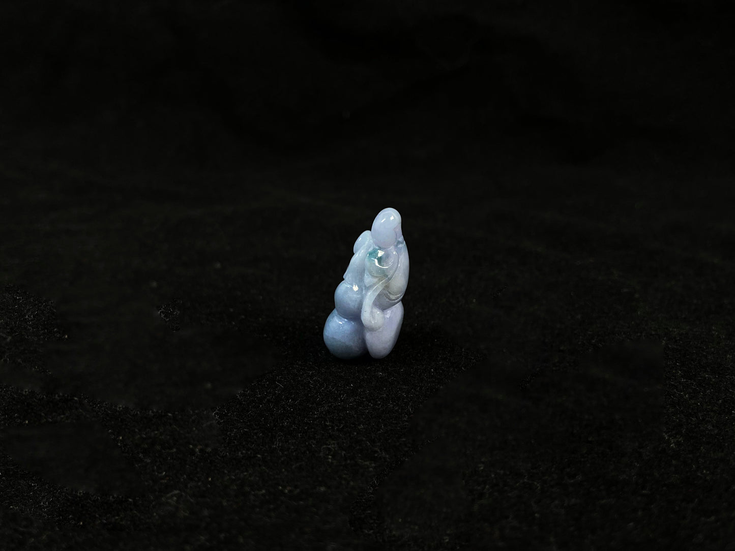 A violet jade carving of three entwined gourds, kissed by wisps of green.