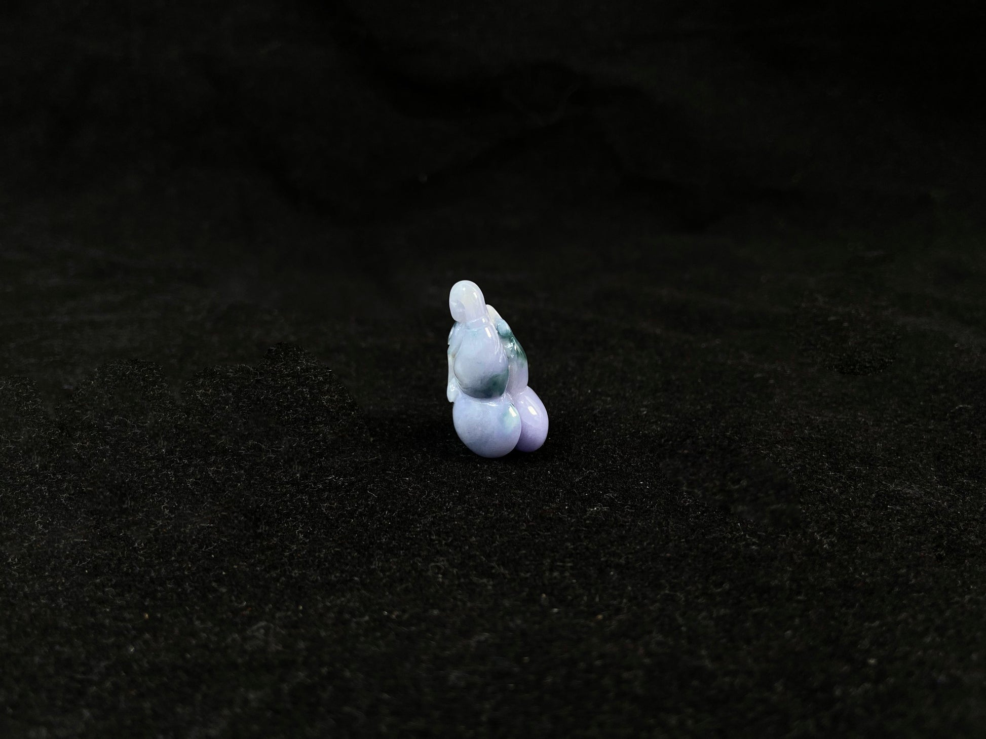 A violet jade carving of three entwined gourds, kissed by wisps of green.