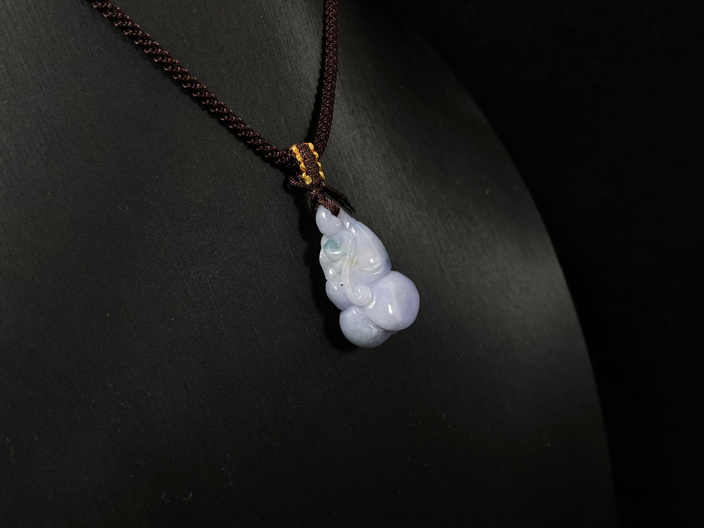 A violet jade carving of three entwined gourds, kissed by wisps of green.