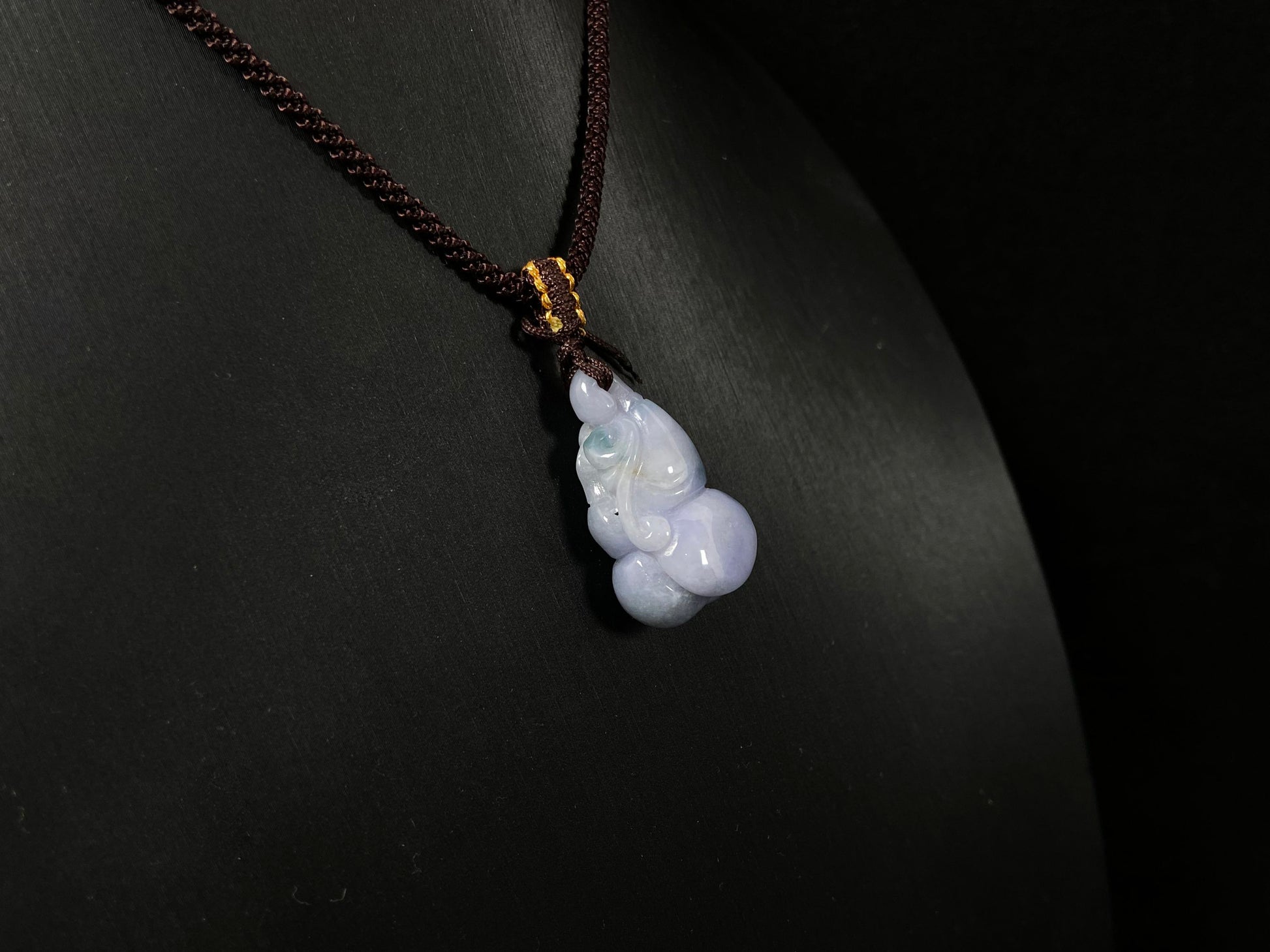 A violet jade carving of three entwined gourds, kissed by wisps of green.