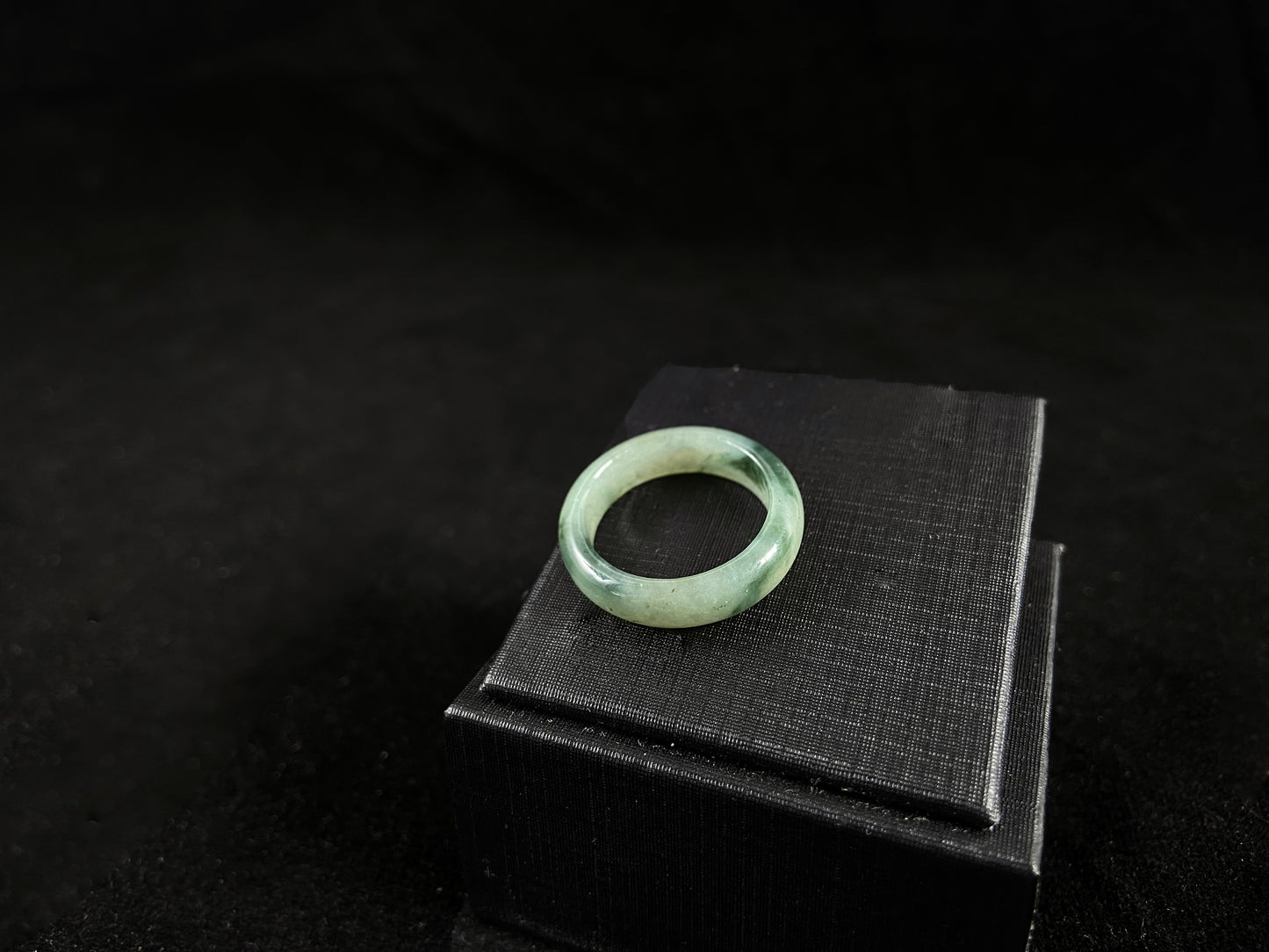 A pale green jadeite ring with elegant dark grey-green accents.