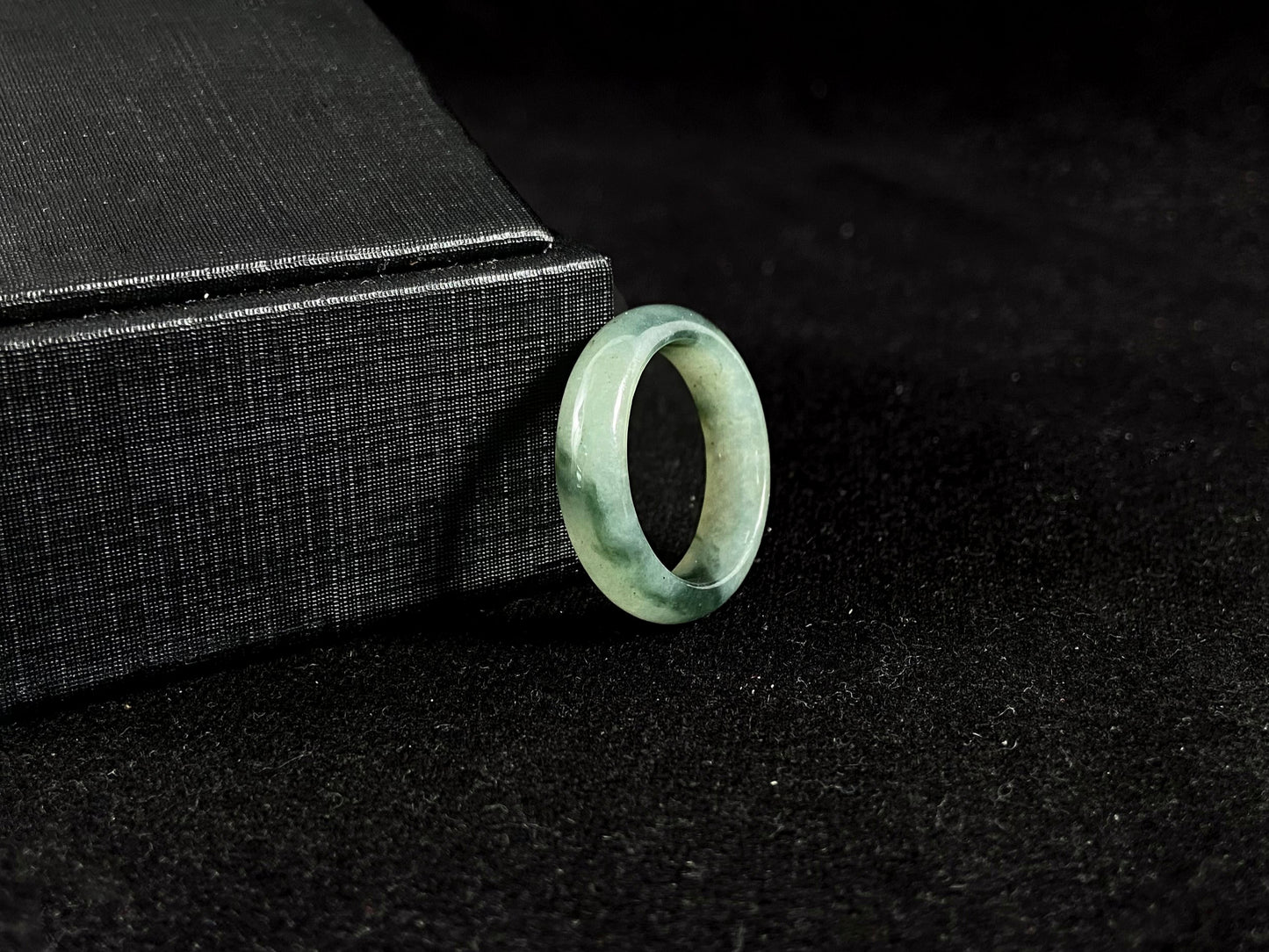 A pale green jadeite ring with elegant dark grey-green accents.
