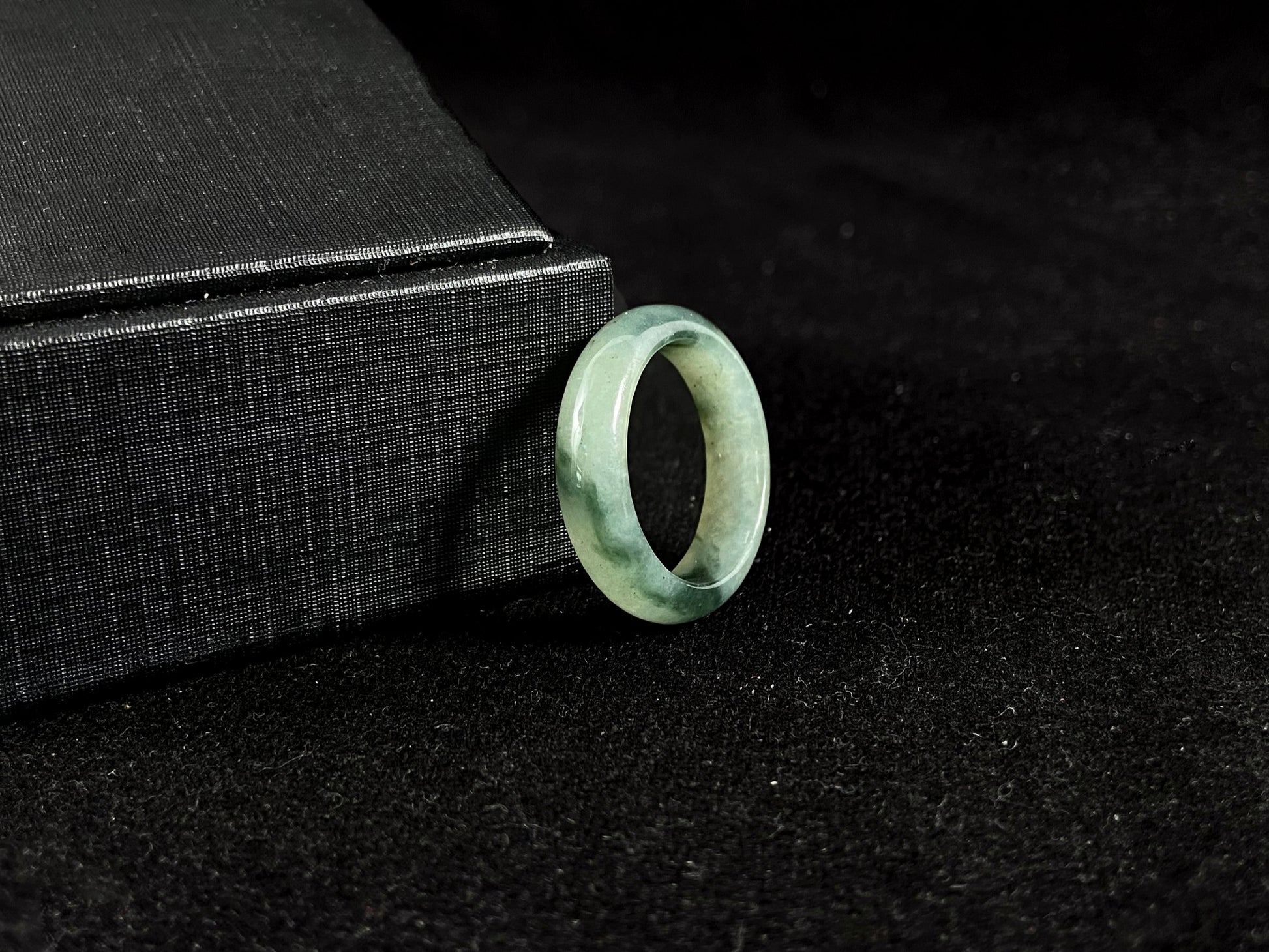 A pale green jadeite ring with elegant dark grey-green accents.