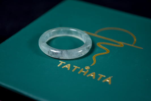 Clear gemstone ring on a green surface with 'TATHATA' branding.