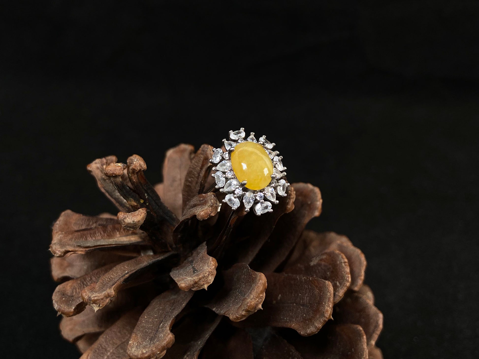 Stunning oval yellow jade is showcased in a diamond paved 925 silver setting.