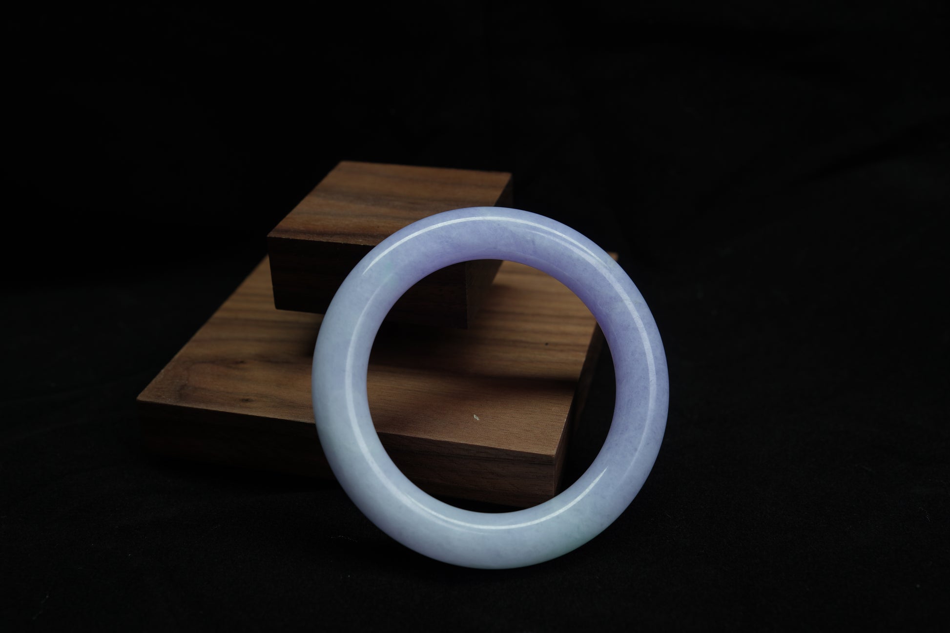 A natural violet jadeite round bangle displayed on a wooden stand, symbolizing elegance and serenity.